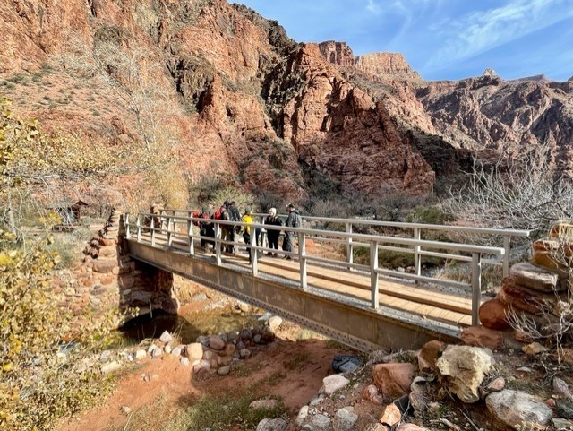 A group of people stand on a foot bridge over a creek.