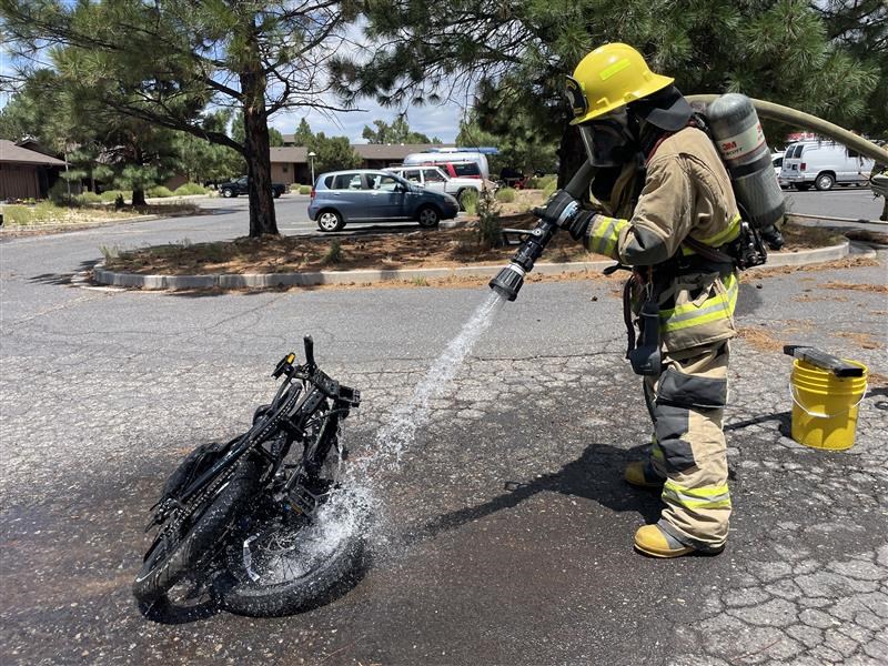 A firefighter hoses down a black e-bike in a parking lot.