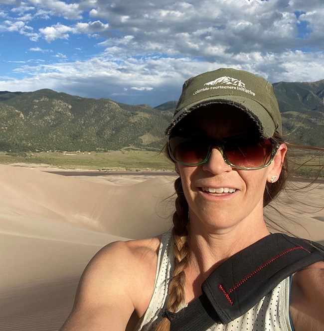 Lisa Devore A woman in hat and sunglasses smiles at the camera with grassy hills in the distance behind her.