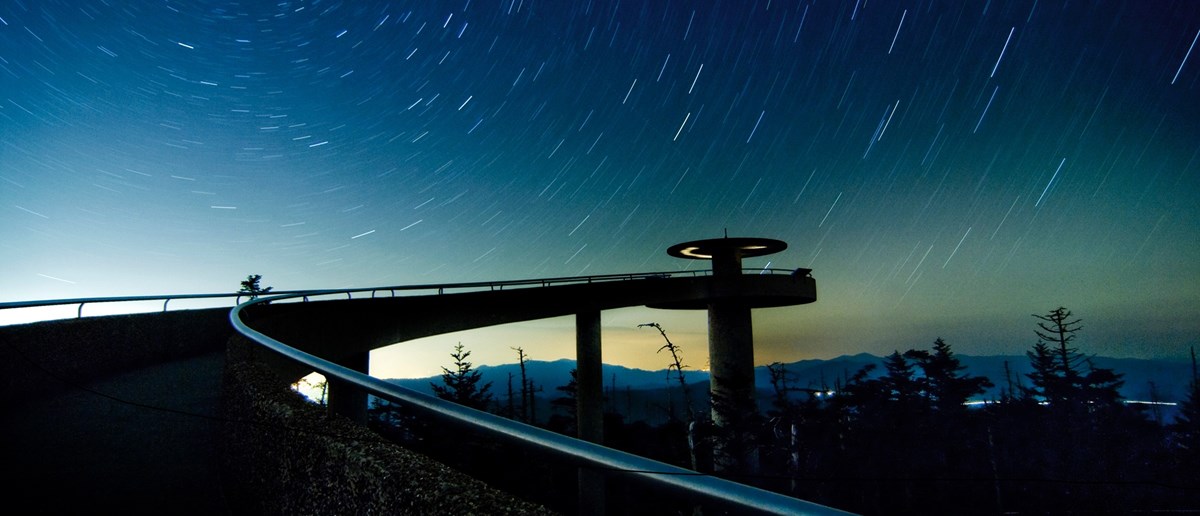 Time capture of stars circling around a night sky above an observation tower in the mountains