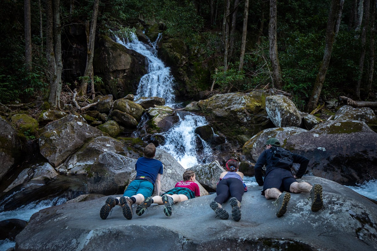 Hikers laying on a boulder while watching a waterfall