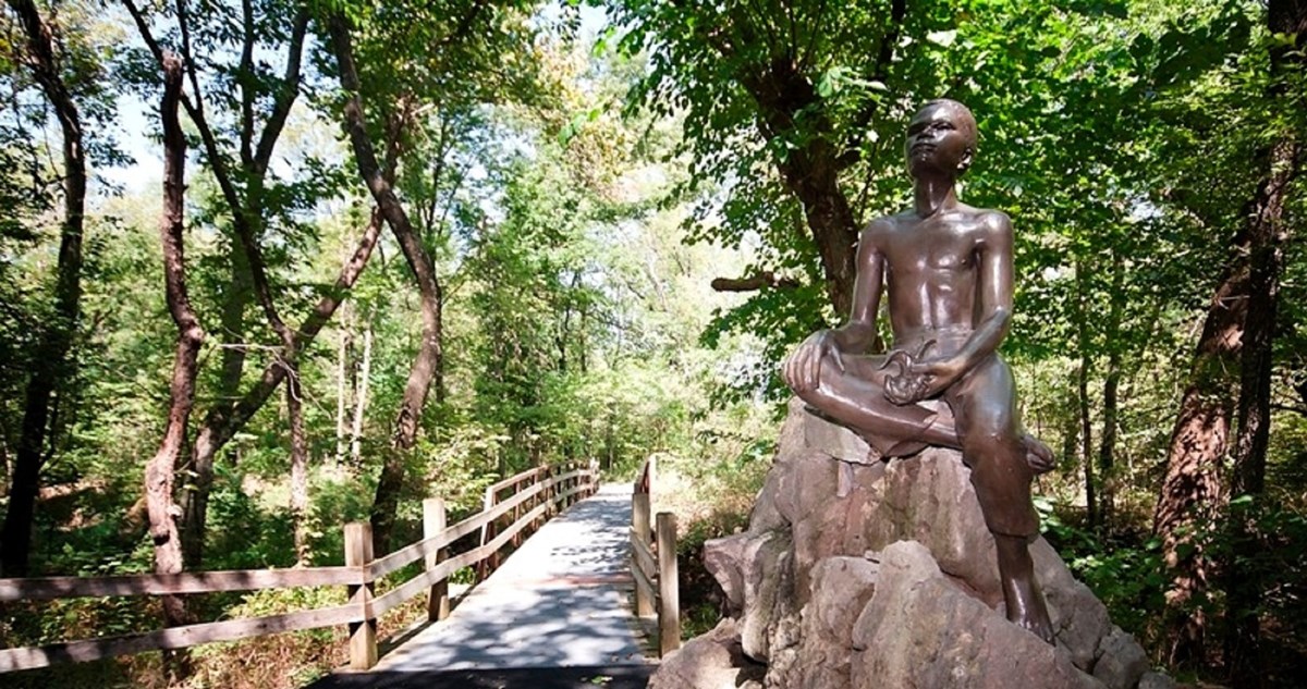Statue of George Washington Carver as a boy sitting on a rock near a nature trail in the woods