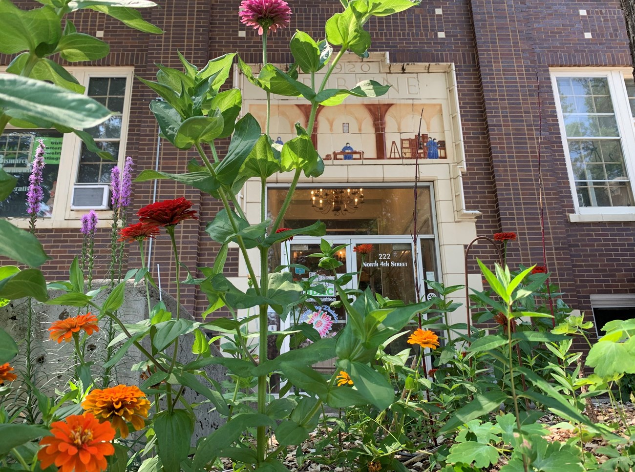 Northern Plains NHA Pollinator Garden Close-up of various multi-colored flowers in a garden. An historic brick and stone building stands in background.