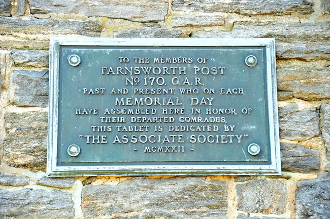 Small, greenish, rectangular metal plaque, with inscription letters, set on stone side of church