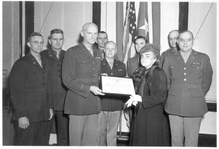 a group of men in uniform stand while one presents a certificate to a woman