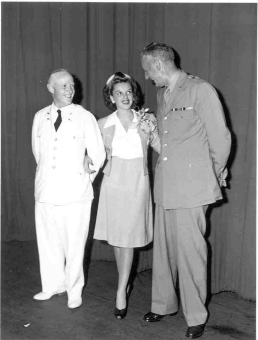 two men in uniform stand linking arms with a young Judy Garland
