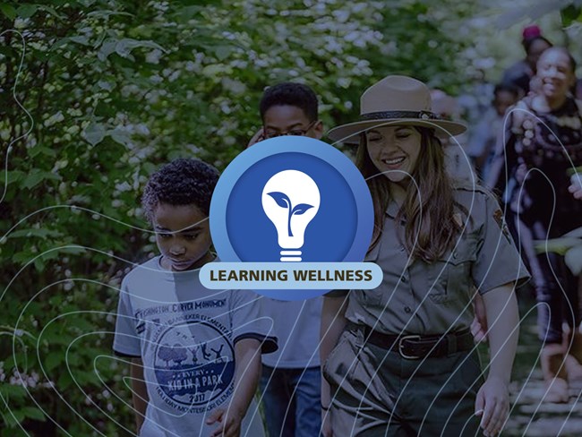 A circular blue graphic with a lightbulb containing a plant in the center and the words Learning Wellness, graphic is on top of blue tinted photo of a park ranger and kids on a trail.
