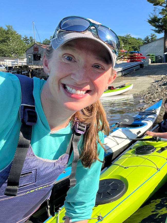 a smiling woman stands among kayaks on land a smiling woman stands among kayaks on land