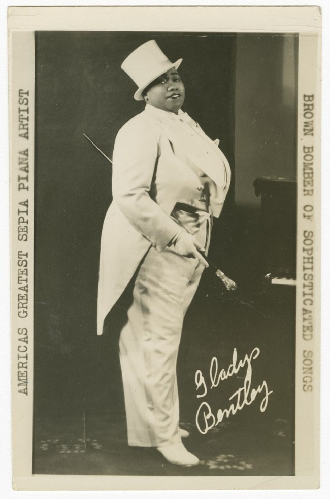 Postcard of Gladys Bentley dressed in a men's  tuxedo and hat. The phrase: "America's Greatest Sepia Player" and "The Brown Bomber of Sophisticated Songs" printed down the sides.