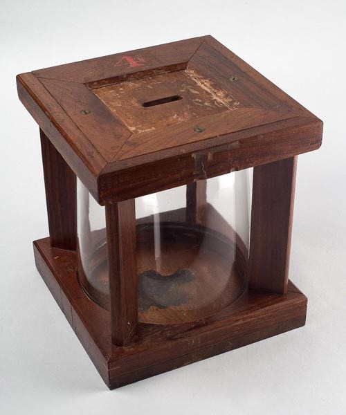 Glass jar inside a wooden box with a hole on top to allow for ballots to be deposited into the glass jar.