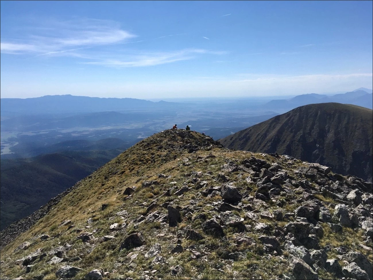 Two scientists on a rocky mountain summit with vast blue sky beyond. Two scientists on a rocky mountain summit with vast blue sky beyond.