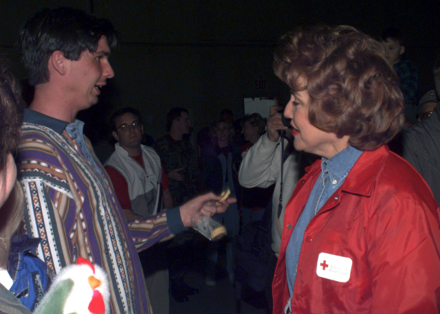 A man wearing a colorful sweater talks to a woman wearing a red cross jacket.