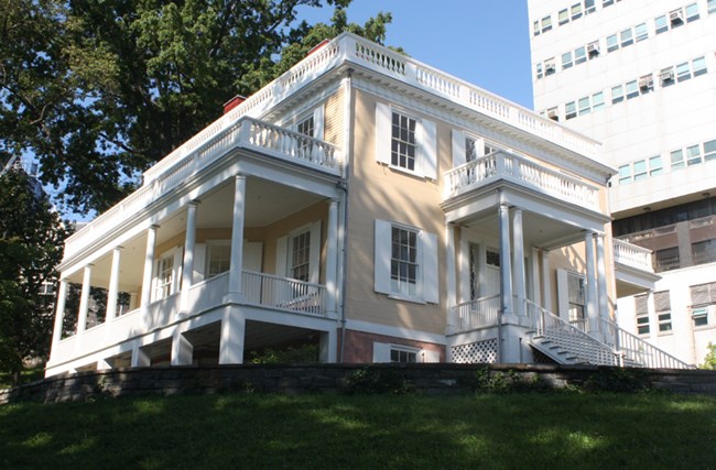 Hamilton Grange, a yellow house with stately porches, sits atop a grassy hill.