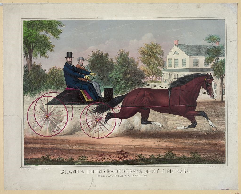 Two men riding in a carriage being pulled by a horse on a dirt road, with trees and a white house in the background.