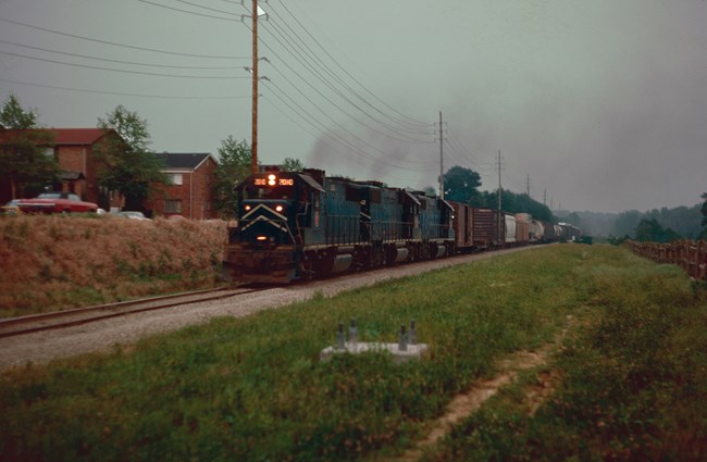 Image of a train on a railroad with an apartment complex in the background.