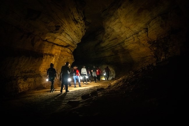 A group of people walk in a dark cave while holding lanterns.