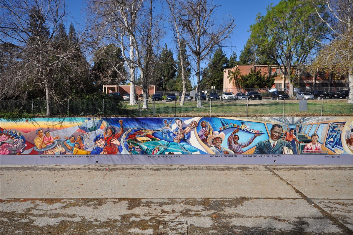 Photograph of a colorful mural painted on a low wall. This section contains depictions of highway construction through Latino neighborhoods, the birth of Rock and Roll, and Civil Rights leaders.