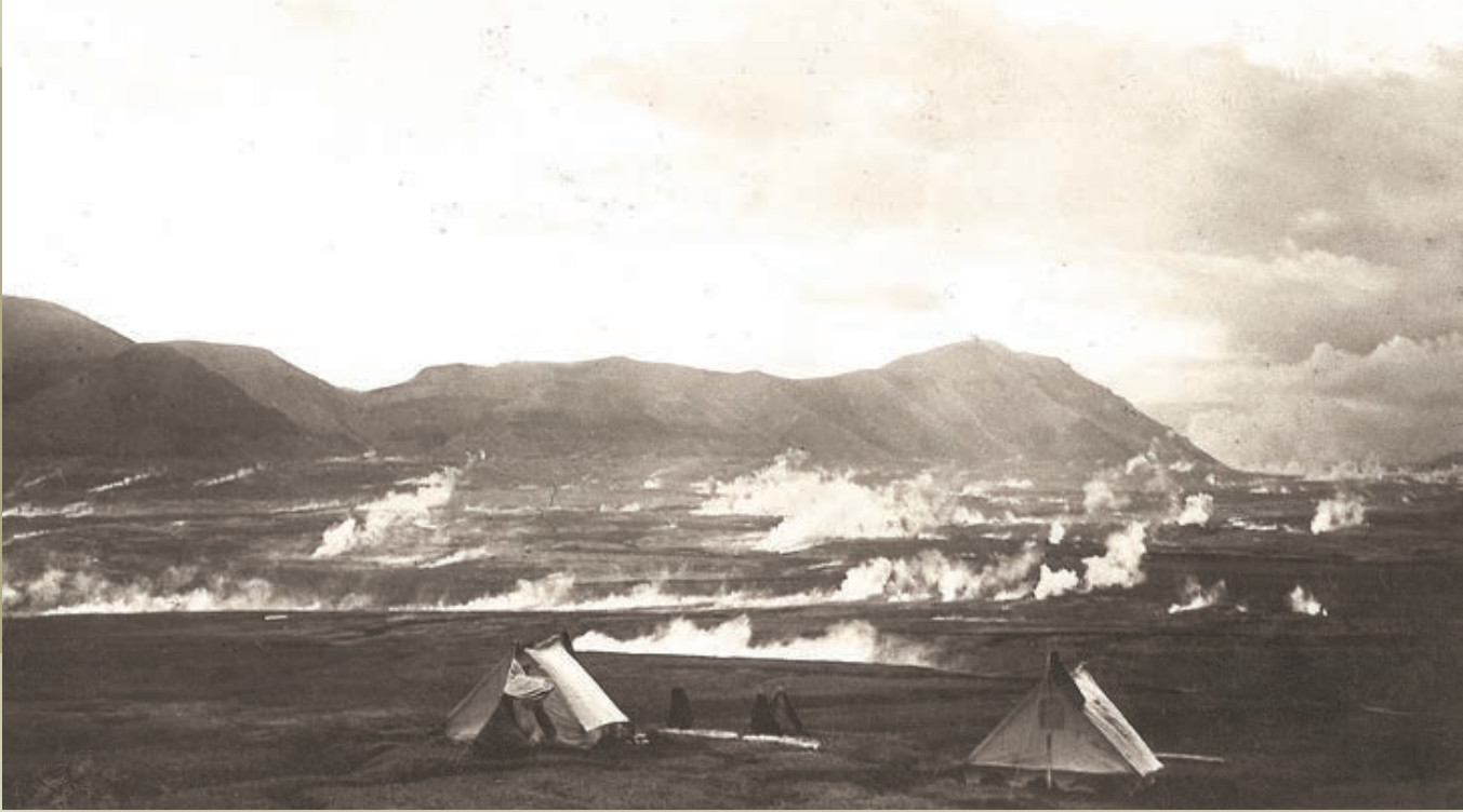 photo of canvas tents set up adjacent to a valley of steaming fumaroles with mountains in the distance
