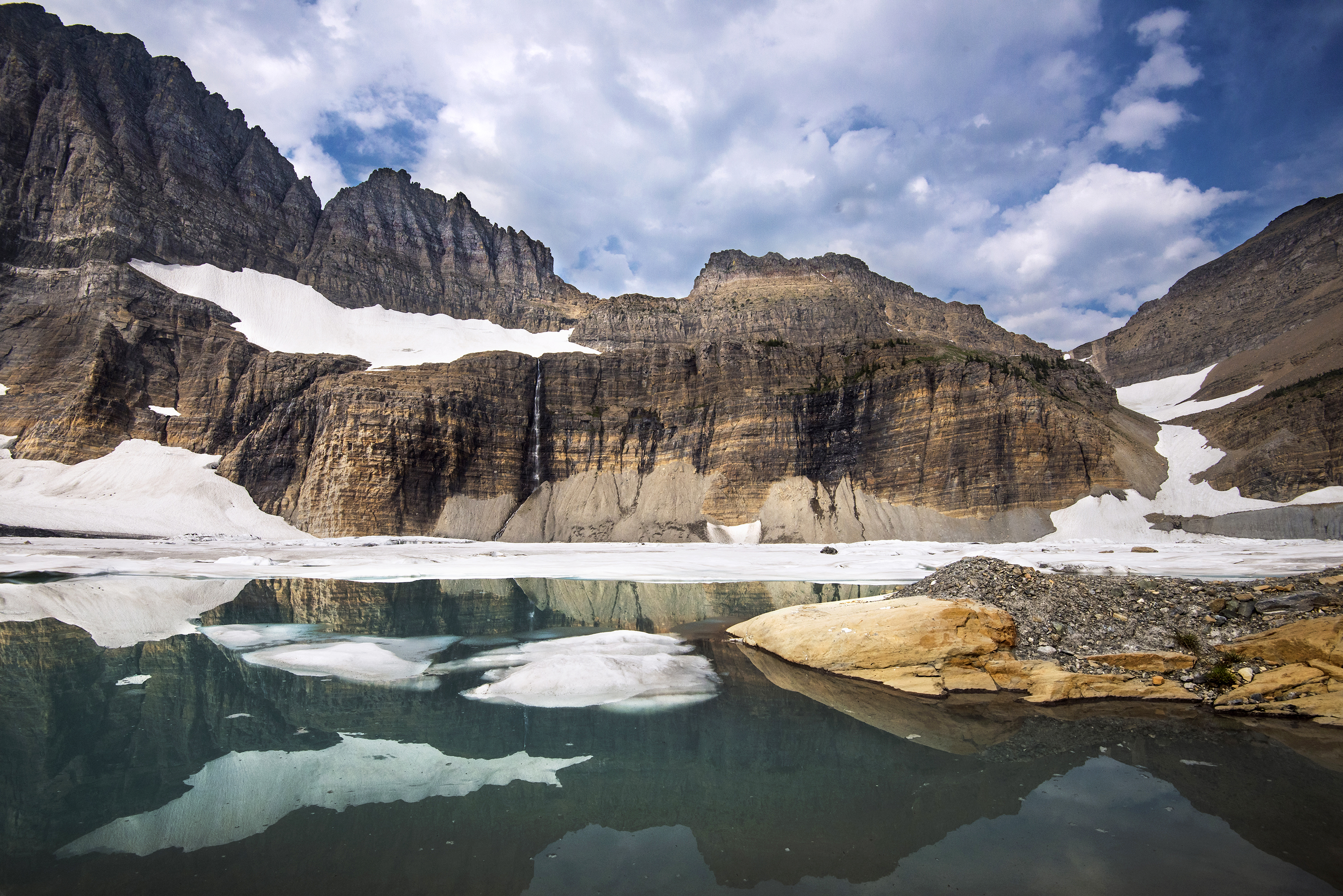 Mountain ridge with glacier, snow, and ice above a teal blue lake