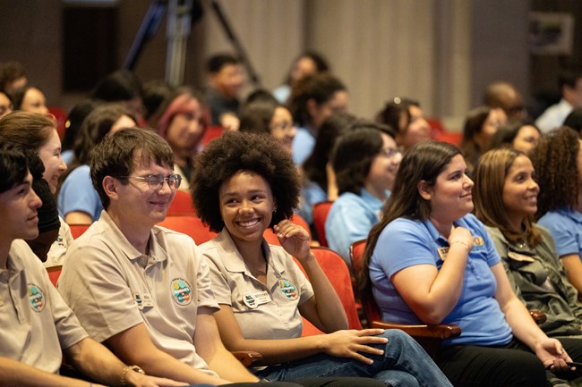Group of individuals listening attentively to a session. They are wearing khaki or blue colored shirts.