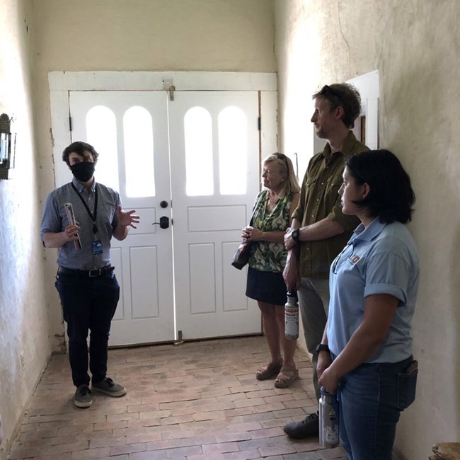 lt= People stand in a hallway of a historic home, listening to a park ranger.