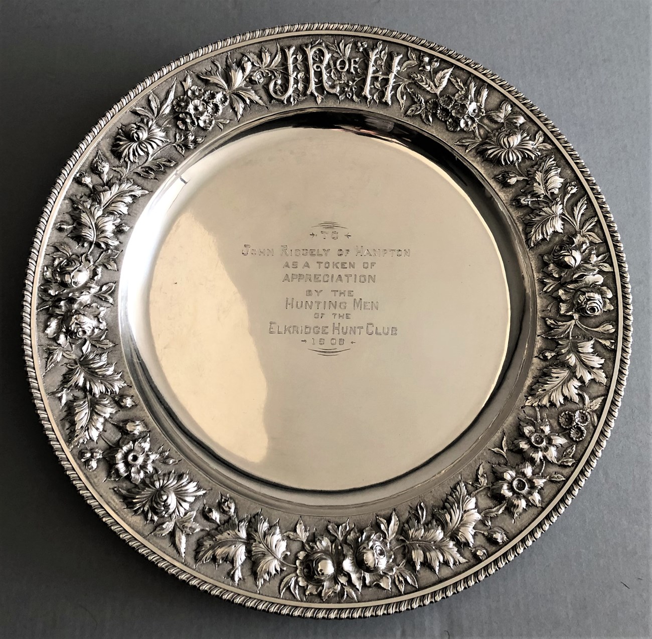 presentation tray_1 A circular silver tray with engraved art around the edges and an inscription in the middle.