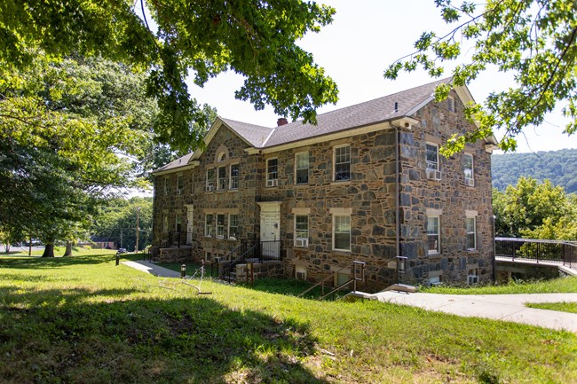 A two-story stone building lined with trees, grass, and sidewalks.