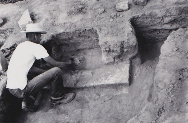 A man excavates the remains of a fireplace in room 102 of Bent's Old Fort, 1954.