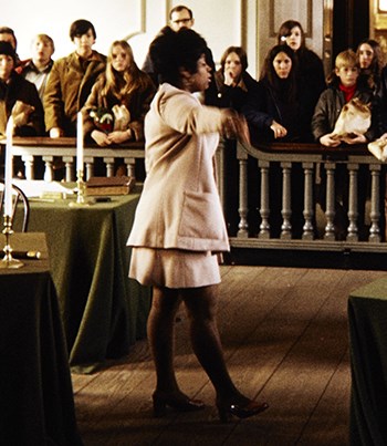 A black woman wearing a tan NPS uniform talks to a group of visitors.