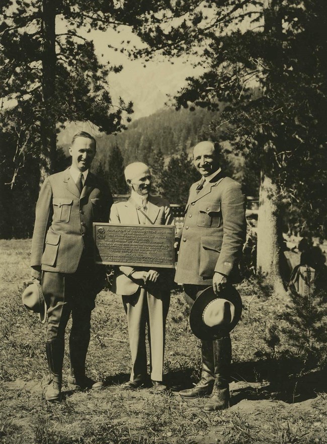 Horace Albright in uniform holding his ranger hat poses outdoors next to Billy Owen and Sam Woodring.