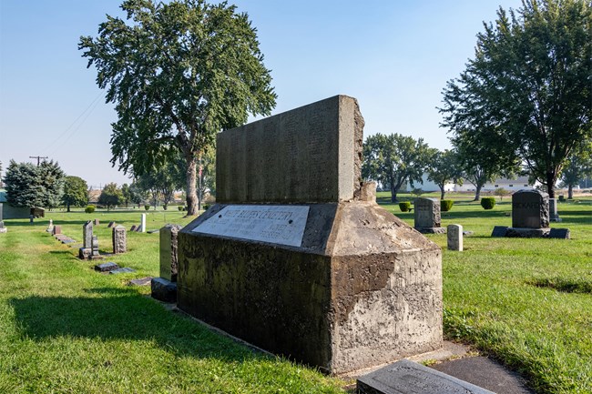 A large grave in the foreground of a manicured cemetery.