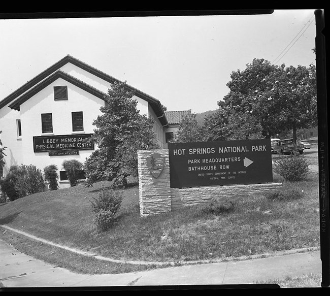 Building With Sign on the Building Reading "Libbey Memorial Physical Medicine Center Visitors Welcome" Sign in Front of the Building Reads "Hot Springs National Park","Park Headquarters","Bathouse Row","United States Department of the Interior","National