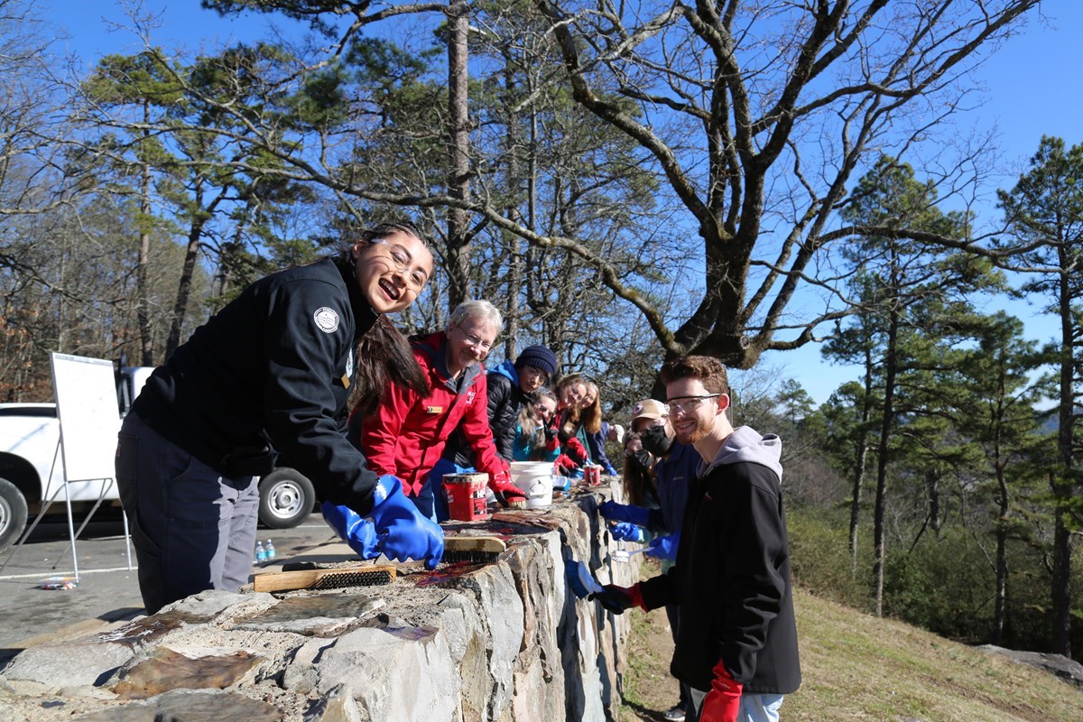 Volunteers use scrubbing brushes to clean graffiti off a stone overlook.