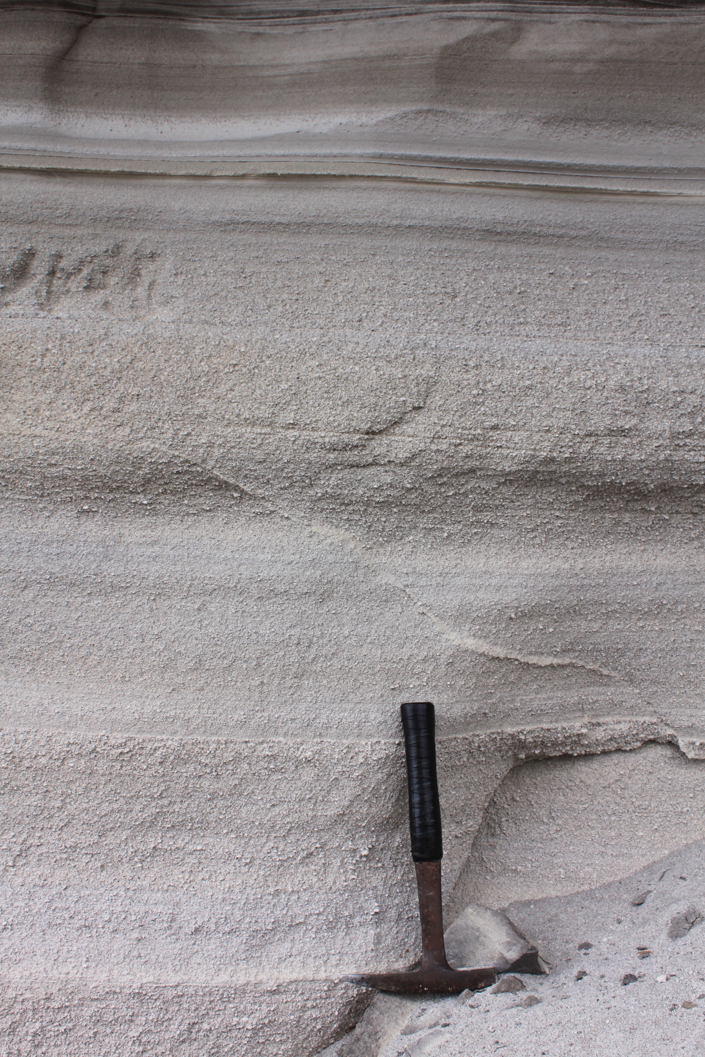 photo of layered, fine-grained sediments with a rock hammer for scale