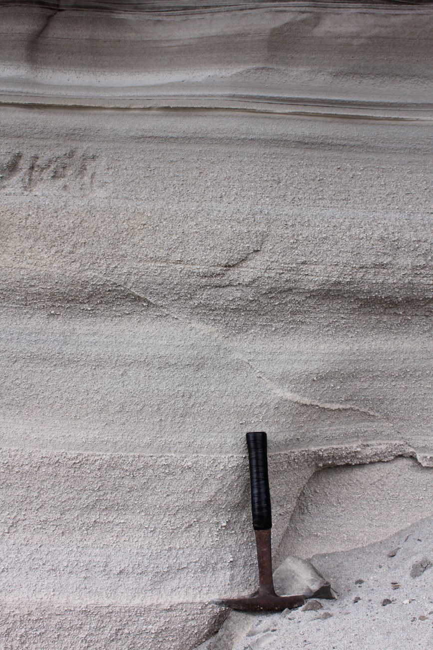 photo of layered, fine-grained sediments with a rock hammer for scale