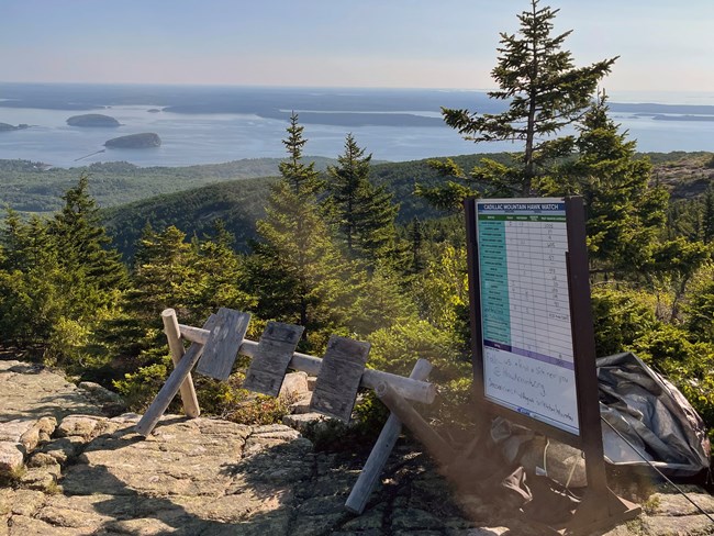 Mountain summit with islands in distance and a large sign in foreground displaying a chart