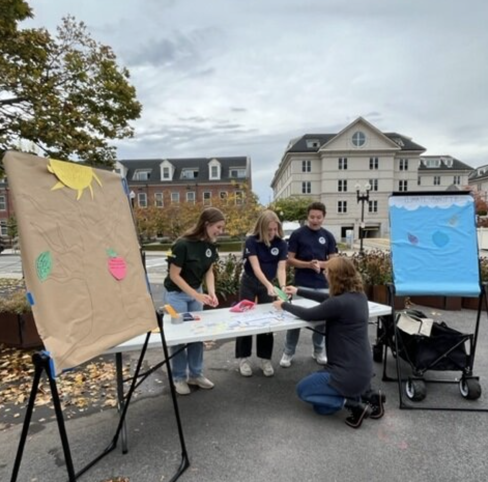 Three Climate Conservation Corps crew members standing behind a table while a visitor writes on paper on the table.