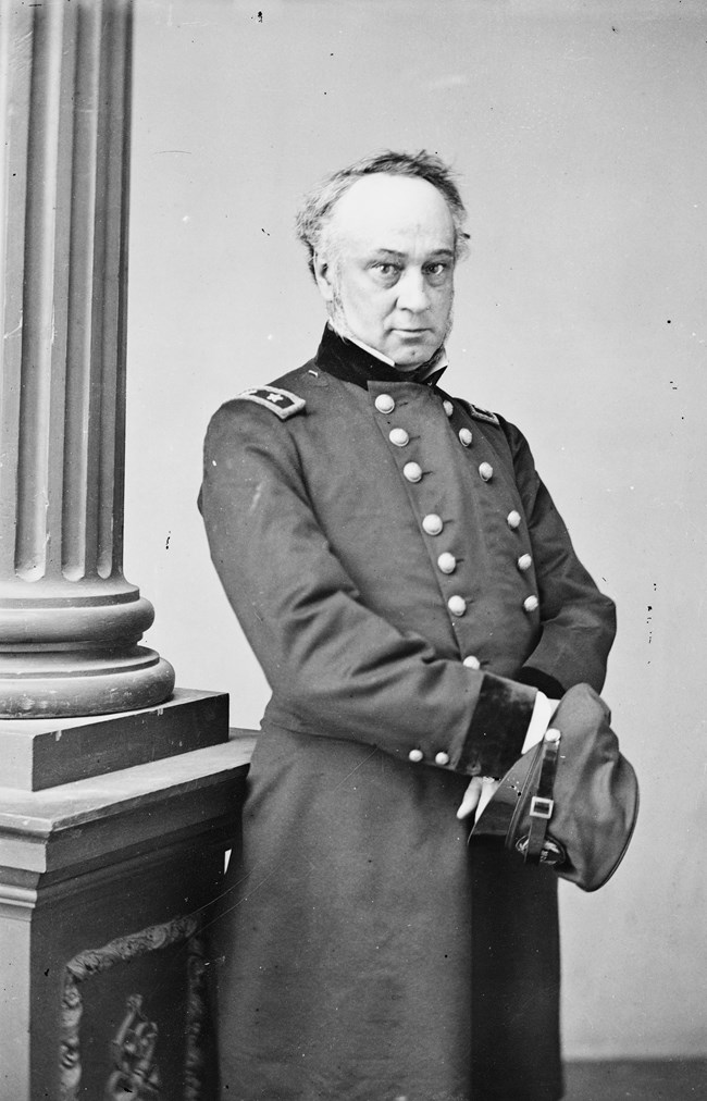 A black and white photograph of a man, standing, in United States military uniform.