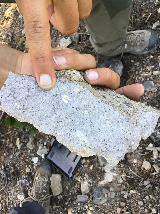 photo of a person's hands holding a rock and pointing to the fine particles