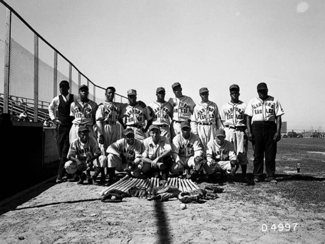 The Hanford Eagles Black and white photo of African American men in baseball uniforms in two rows. Bats and gloves are laid out in front of them.