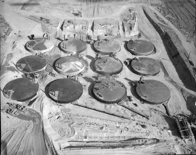 Historic aerial image of 12 large round tanks placed in 3x4 grid, buried except for the tops.