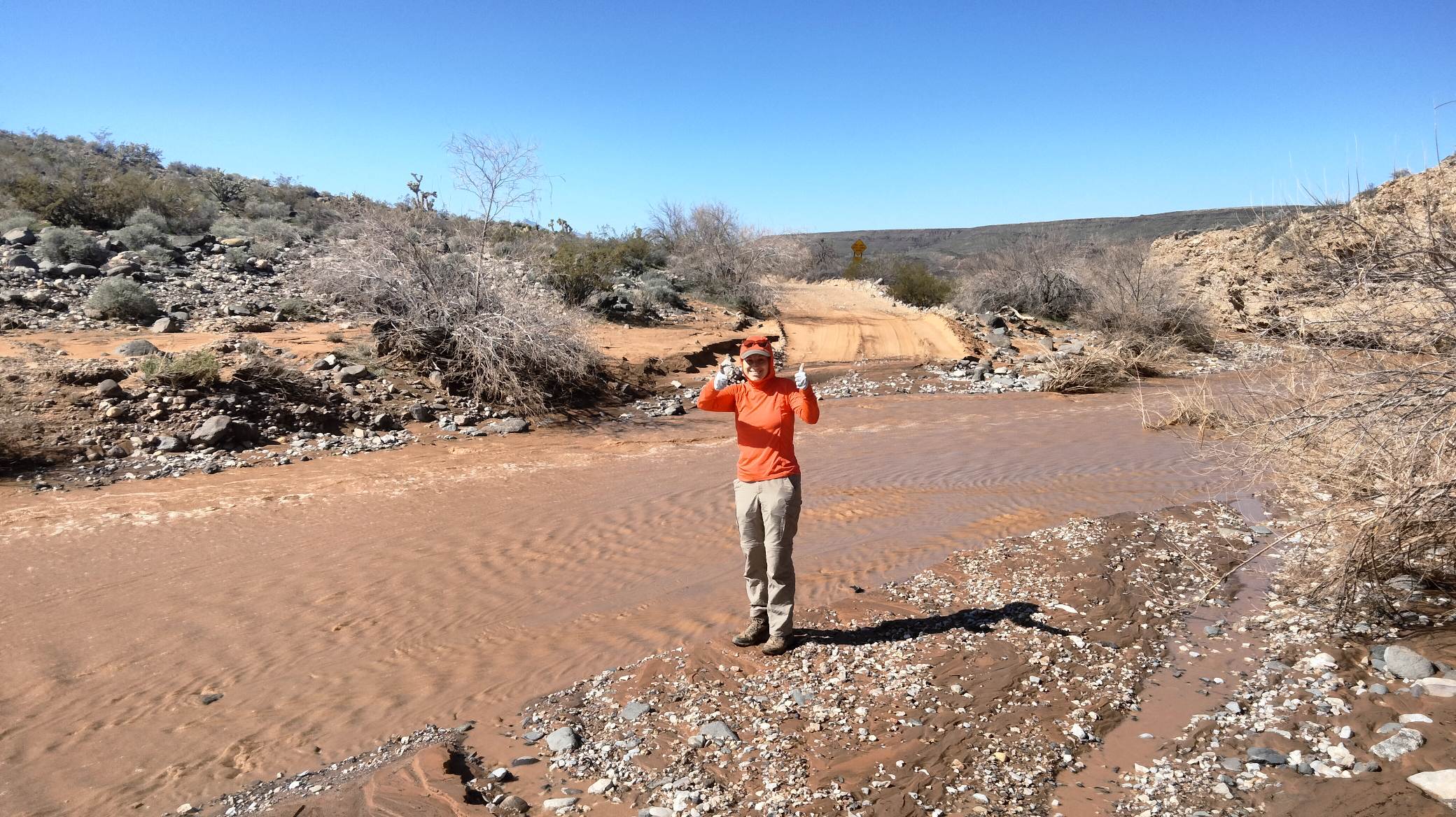 Water was abundant in Parashant National Monument this spring. Woman gives thumbs up as she stands next to a wash flowing with muddy water.