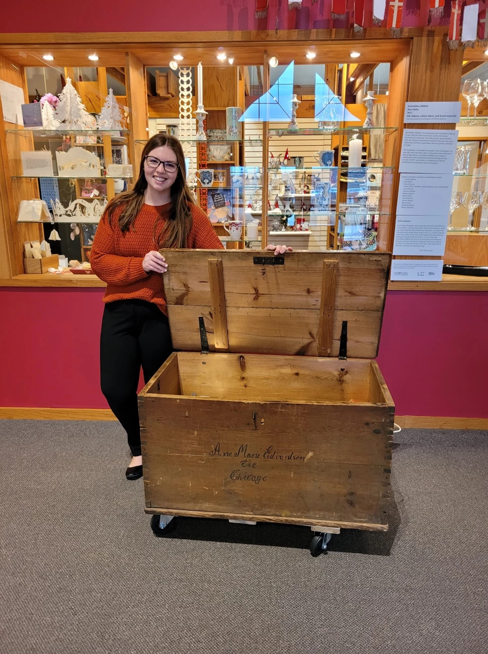 Hannah teaching students about immigration at the Museum of Danish America Hannah posing with a museum artifact behind a museum collection at the Museum of Danish America