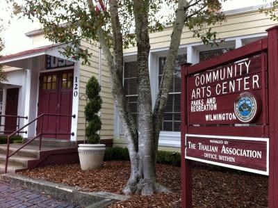 Front entrance of the Hannah Block Historic USO/Community Arts Center. There is a sign naming the building, a tree next to the sign, and a potted plant next to the entrance stairs.