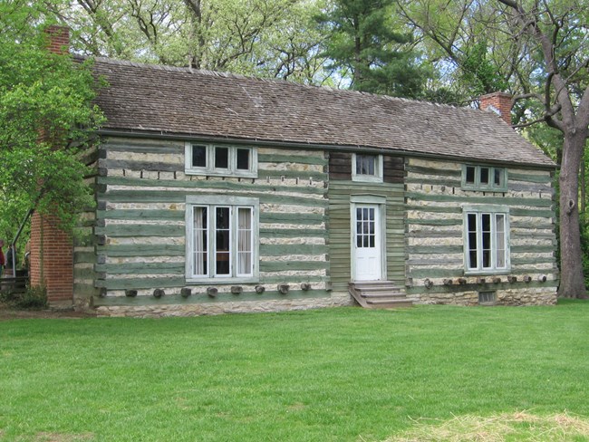 brown and green log cabin with green trees in background.