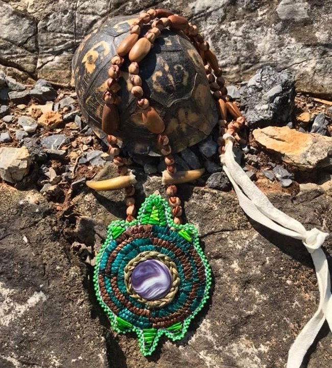 A beaded necklace with a turtle medalion resting on a turtle shell.