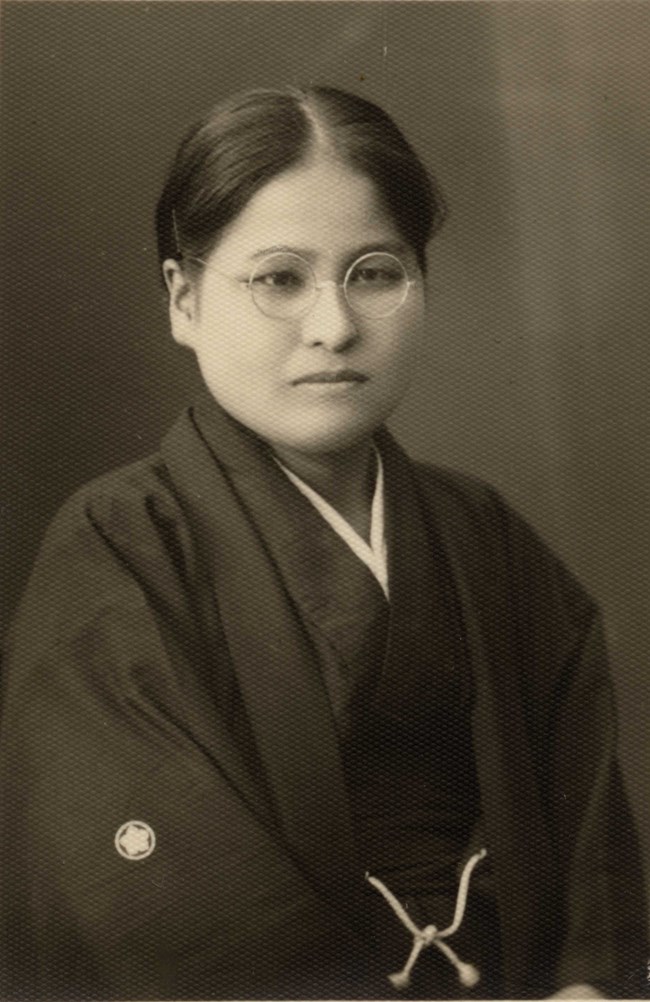 Asian woman in dark kimono, wearing classes, in a formal portrait