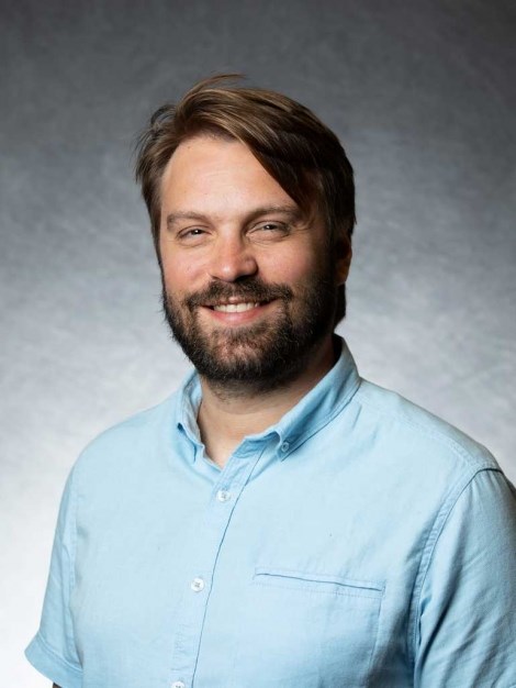 Dr. Stephen Hausmann Headshot of a white man with brown hair and a beard wearing a blue shirt