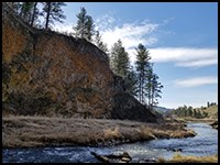 Looking down Hawk Creek from the pool adjacent to the waterfall, with a 30' cliff on the left covered in lichen. The creek winds through a shallow valley beyond.