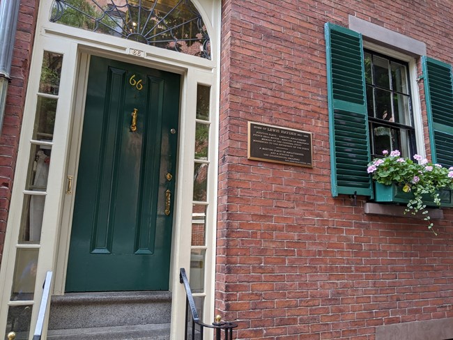 Brick townhouse with a bright green door and a green flower box underneath window.
